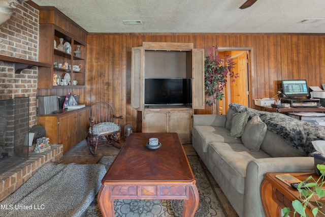 living room with ceiling fan, wooden walls, a textured ceiling, and a fireplace