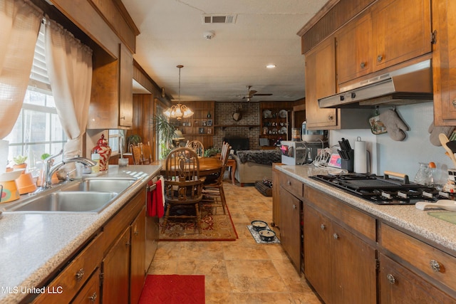 kitchen with pendant lighting, sink, black gas cooktop, a brick fireplace, and ceiling fan with notable chandelier