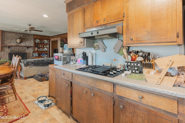 kitchen with ceiling fan, black gas stovetop, and a brick fireplace