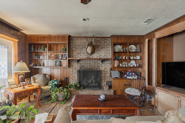 living room with built in features, a textured ceiling, a brick fireplace, and wood walls