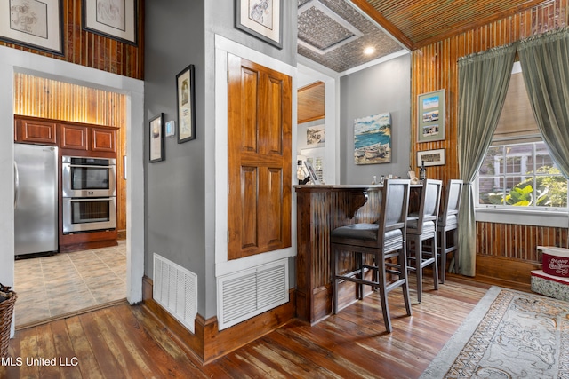 bar with appliances with stainless steel finishes, hardwood / wood-style floors, wooden walls, and ornamental molding