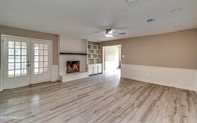 unfurnished living room with light hardwood / wood-style flooring, a brick fireplace, built in features, a textured ceiling, and ceiling fan