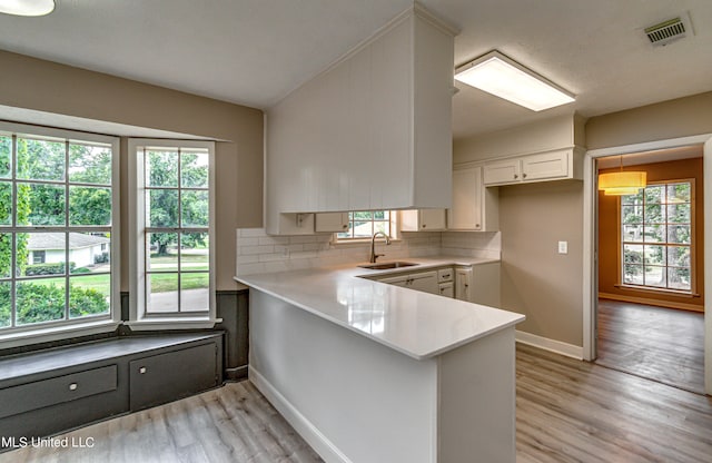 kitchen featuring light hardwood / wood-style flooring, kitchen peninsula, backsplash, sink, and white cabinets