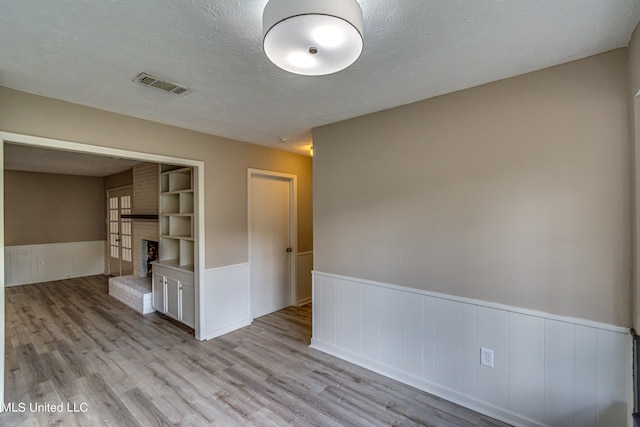 empty room featuring light hardwood / wood-style floors, a textured ceiling, a brick fireplace, and built in shelves