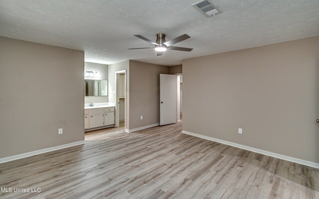 unfurnished bedroom featuring ceiling fan, a textured ceiling, light wood-type flooring, ensuite bath, and sink