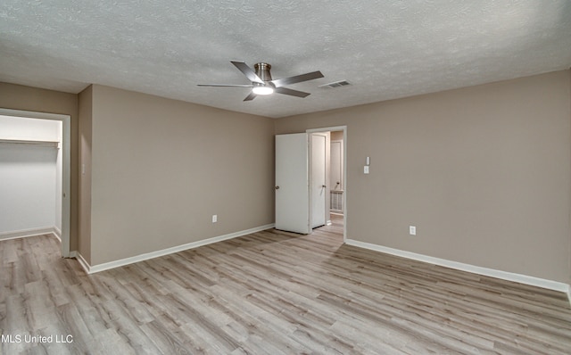 unfurnished bedroom with a spacious closet, a textured ceiling, a closet, ceiling fan, and light hardwood / wood-style flooring