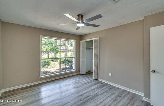 unfurnished bedroom with light hardwood / wood-style flooring, a textured ceiling, a closet, and ceiling fan