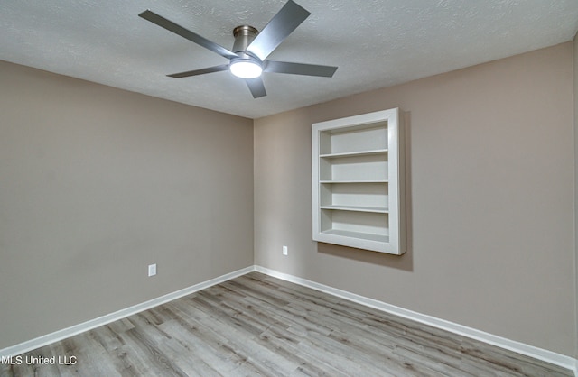 empty room with light hardwood / wood-style flooring, a textured ceiling, built in shelves, and ceiling fan