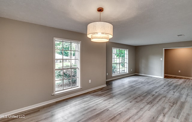 unfurnished room with a textured ceiling, hardwood / wood-style flooring, and a healthy amount of sunlight