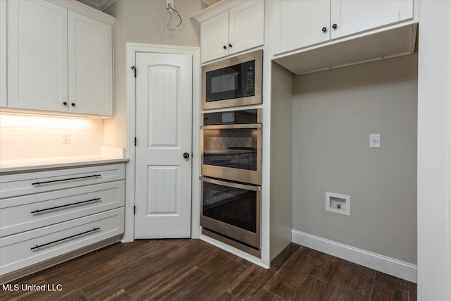 kitchen with dark wood-type flooring, stainless steel double oven, light countertops, built in microwave, and white cabinets