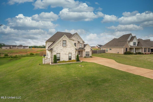 french provincial home featuring concrete driveway, brick siding, fence, and a front lawn