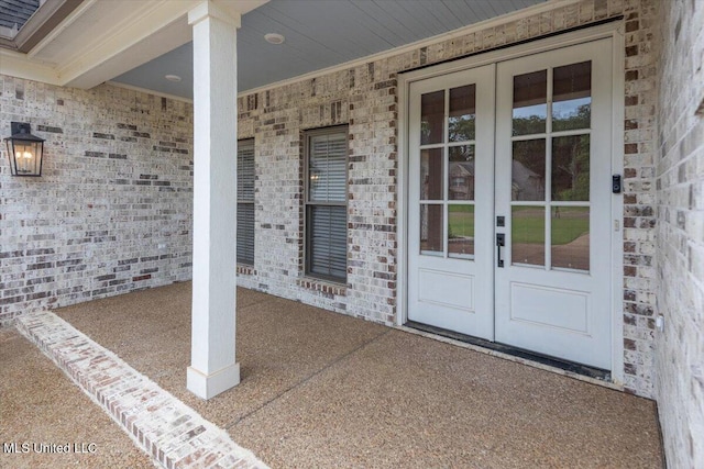 view of exterior entry with covered porch, brick siding, and french doors