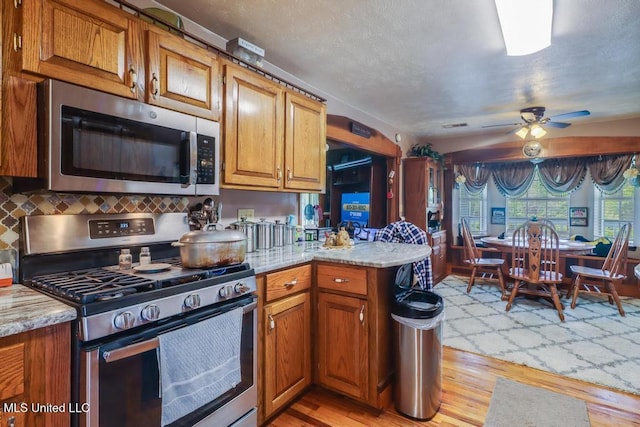 kitchen featuring ceiling fan, appliances with stainless steel finishes, brown cabinetry, a peninsula, and light wood-type flooring