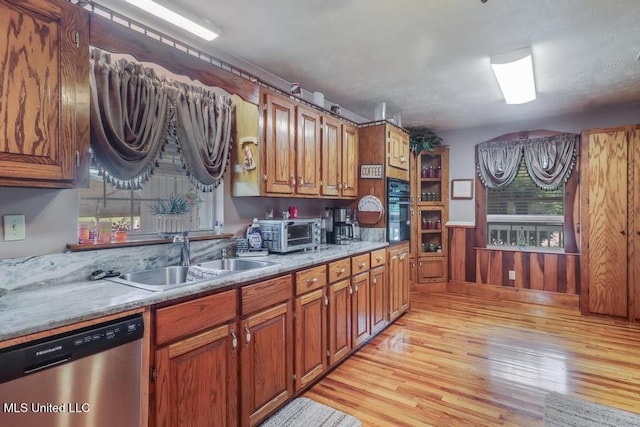 kitchen with brown cabinets, dishwasher, a sink, light wood-style floors, and oven
