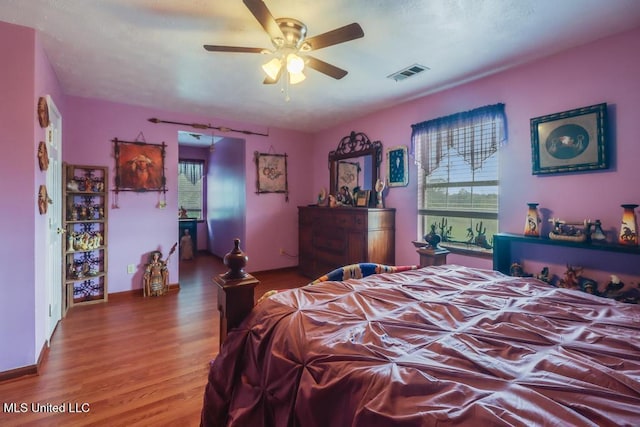 bedroom featuring a ceiling fan, visible vents, multiple windows, and wood finished floors
