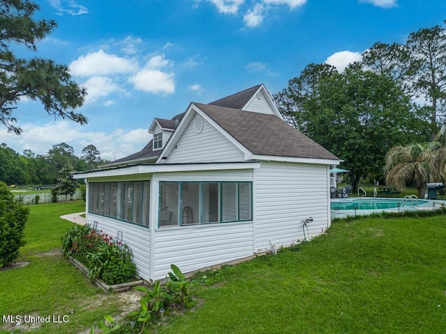 view of property exterior featuring a lawn, a sunroom, roof with shingles, and an outdoor pool