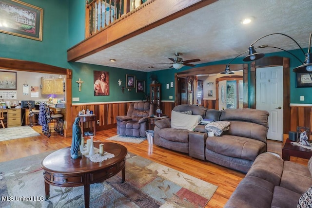 living room with wooden walls, a ceiling fan, wainscoting, and wood finished floors