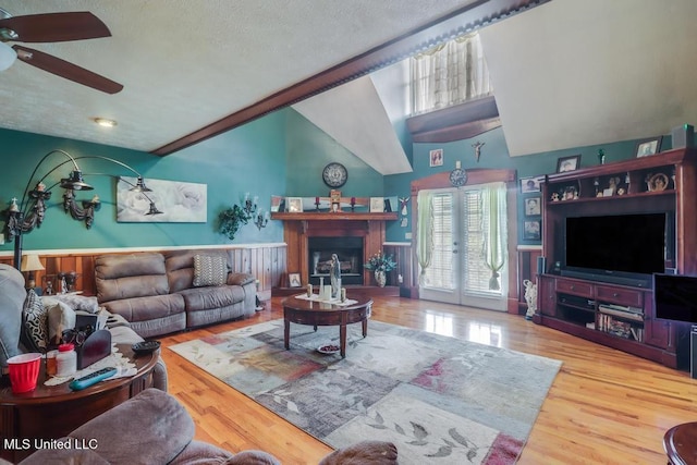 living room featuring a wainscoted wall, ceiling fan, a fireplace, and wood finished floors