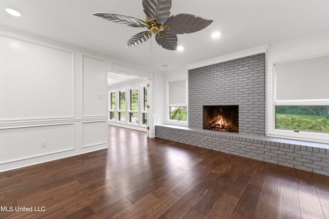 unfurnished living room with crown molding, ceiling fan, a brick fireplace, and dark hardwood / wood-style flooring