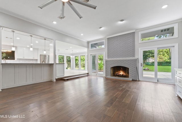 unfurnished living room with dark hardwood / wood-style flooring, ornamental molding, ceiling fan, and a brick fireplace