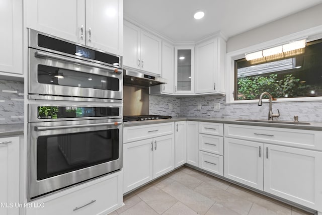 kitchen with sink, light tile patterned flooring, white cabinetry, stainless steel appliances, and decorative backsplash