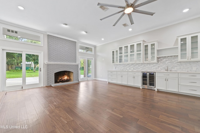 unfurnished living room featuring wet bar, ornamental molding, beverage cooler, a fireplace, and dark hardwood / wood-style flooring