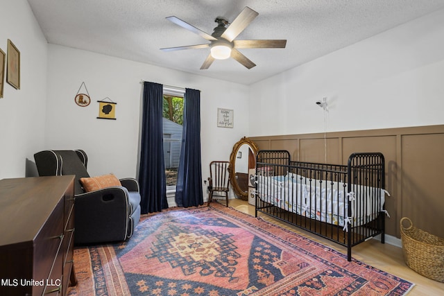 bedroom featuring a textured ceiling, hardwood / wood-style flooring, a crib, and ceiling fan