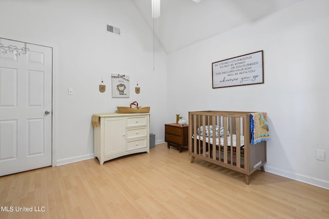 bedroom with a nursery area, high vaulted ceiling, and light hardwood / wood-style floors