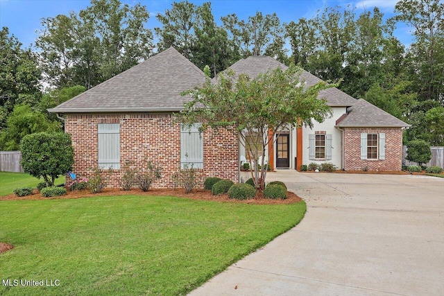 view of front of property featuring driveway, brick siding, a front lawn, and roof with shingles