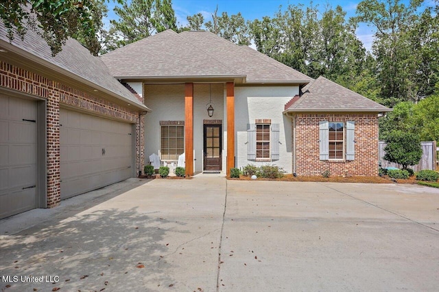 view of front of property featuring a garage, driveway, brick siding, and roof with shingles