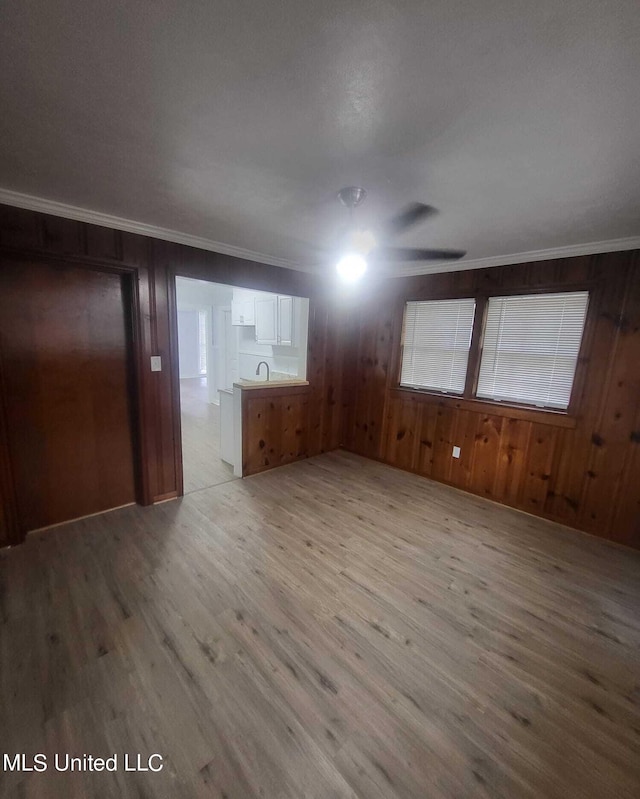 unfurnished living room featuring sink, light hardwood / wood-style floors, ceiling fan, wooden walls, and ornamental molding