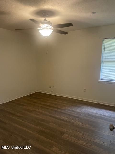 unfurnished room featuring dark wood-style flooring, ceiling fan, baseboards, and a textured ceiling