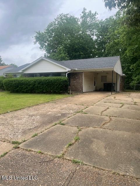 view of side of property featuring concrete driveway, a yard, brick siding, and an attached carport