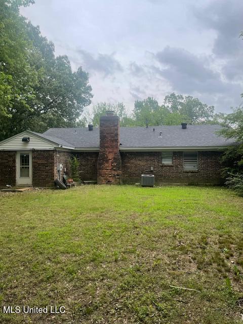 back of property featuring brick siding, a yard, and a chimney