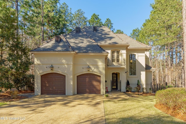 view of front of property with an attached garage, a balcony, fence, driveway, and stucco siding