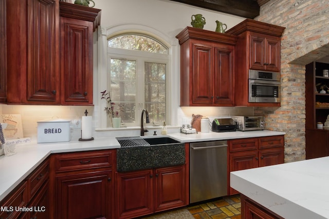 kitchen with reddish brown cabinets, light countertops, backsplash, appliances with stainless steel finishes, and a sink