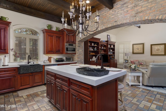 kitchen featuring an island with sink, decorative light fixtures, brick floor, light countertops, and dark brown cabinets