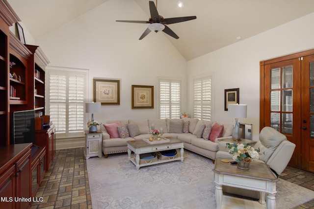 living area with high vaulted ceiling, a ceiling fan, brick floor, and a wealth of natural light