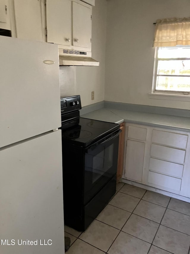 kitchen with freestanding refrigerator, electric range, under cabinet range hood, white cabinetry, and light tile patterned floors