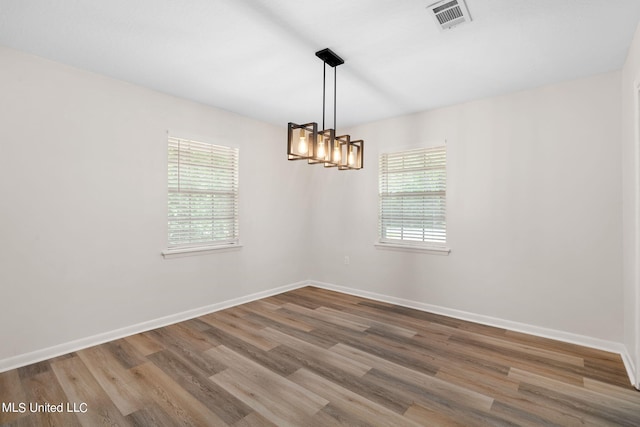 empty room featuring a notable chandelier, plenty of natural light, and hardwood / wood-style floors