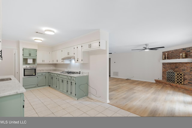 kitchen featuring green cabinets, appliances with stainless steel finishes, a fireplace, light hardwood / wood-style floors, and ceiling fan