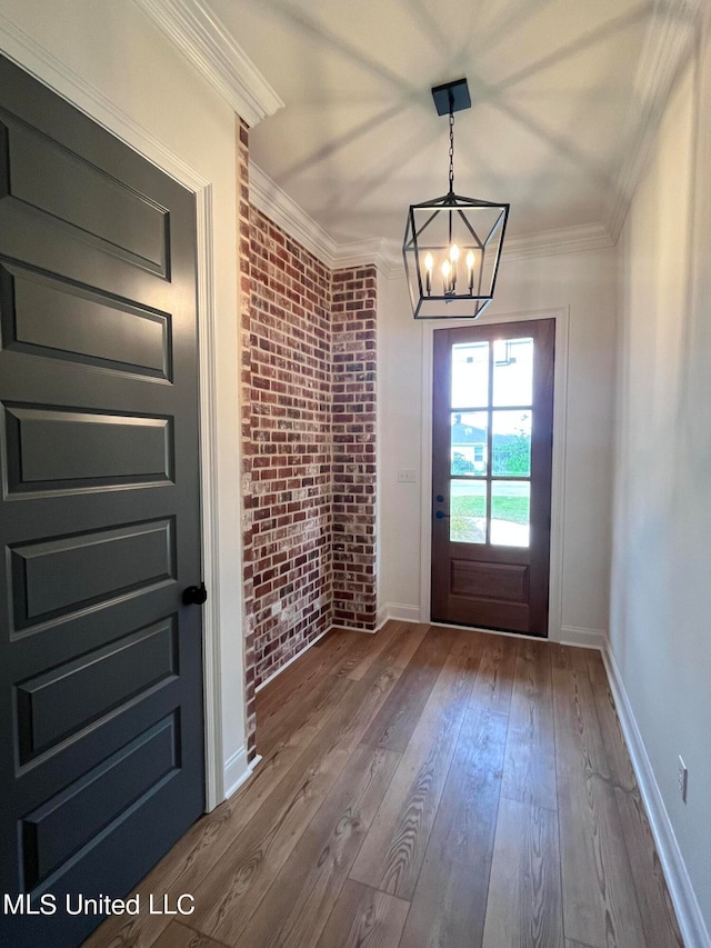 doorway to outside featuring a notable chandelier, wood-type flooring, ornamental molding, and brick wall