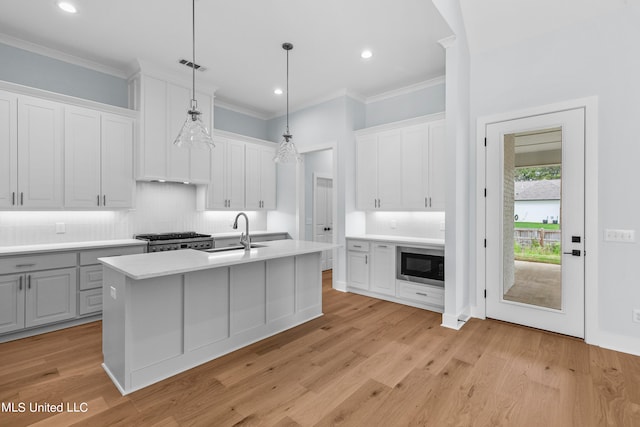 kitchen featuring white cabinetry, light hardwood / wood-style flooring, pendant lighting, and a center island with sink