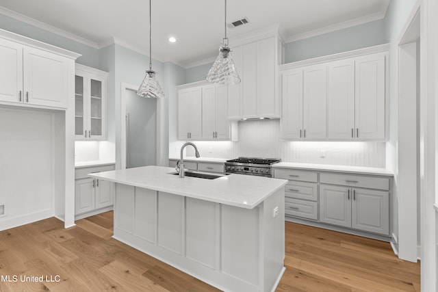 kitchen featuring light hardwood / wood-style flooring, hanging light fixtures, an island with sink, sink, and white cabinetry