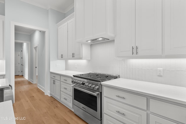 kitchen featuring stainless steel range, white cabinets, crown molding, decorative backsplash, and light hardwood / wood-style flooring