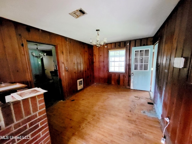 unfurnished dining area featuring hardwood / wood-style flooring, a chandelier, wooden walls, and heating unit