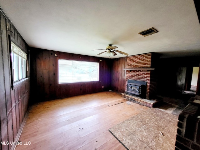 unfurnished living room with a wood stove, light hardwood / wood-style flooring, wooden walls, and ceiling fan