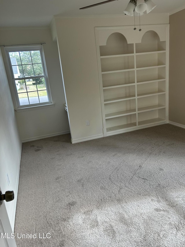 unfurnished room featuring carpet flooring, built in shelves, and ceiling fan