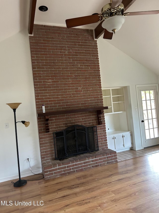 unfurnished living room with lofted ceiling with beams, ceiling fan, wood-type flooring, and a brick fireplace