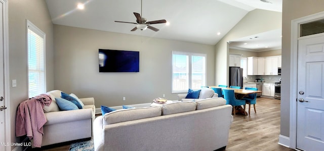 living area with light wood-type flooring, lofted ceiling, ceiling fan, and baseboards